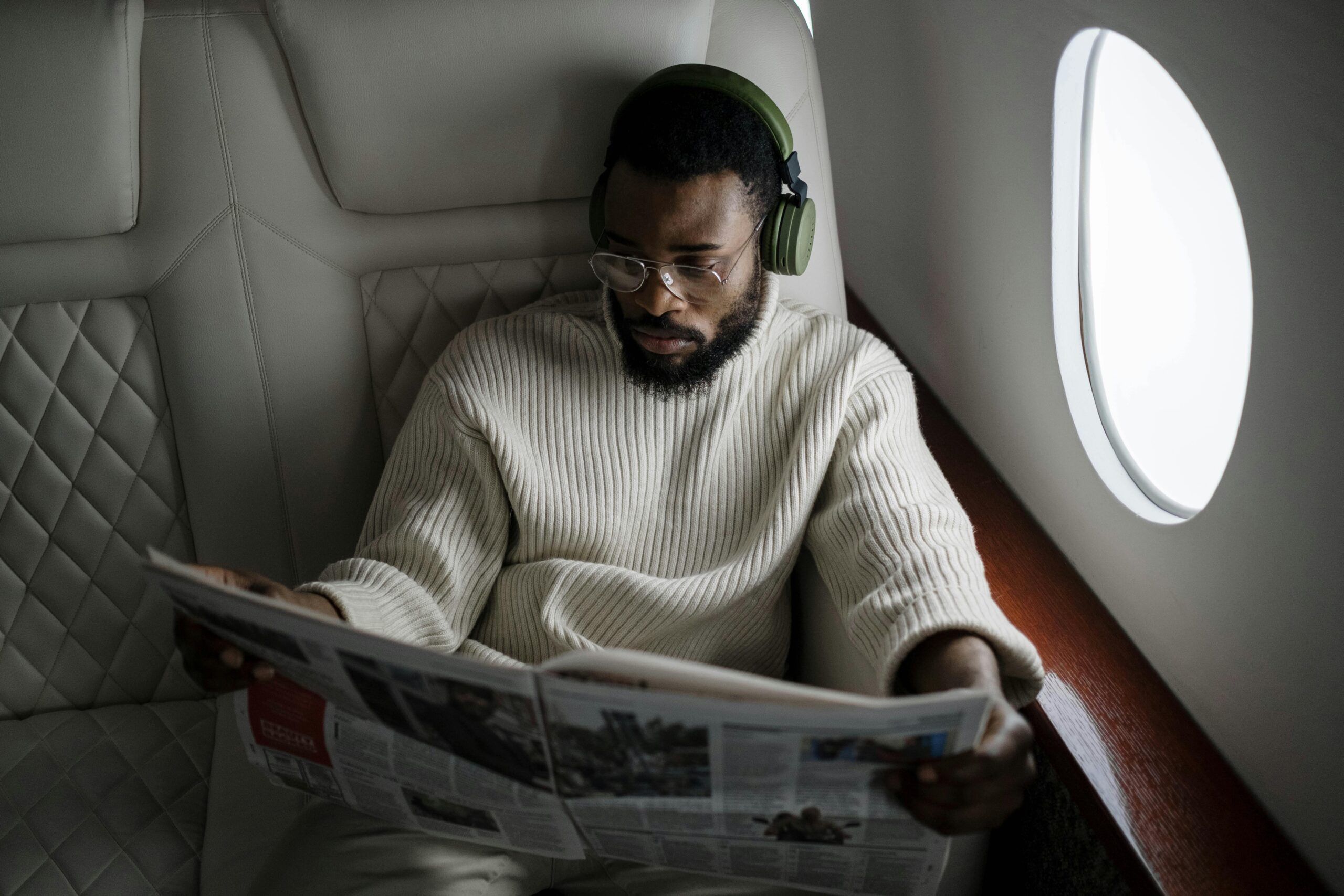 man with headphones reading the paper in a plane